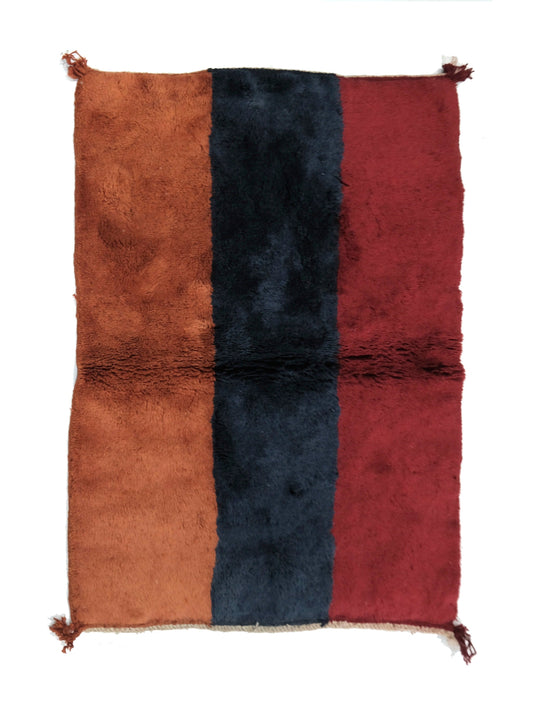 Plush hand-loomed wool rug featuring three wide vertical stripes in terracotta rust, navy blue, and deep burgundy red, with a horizontal central joining seam and small corner tassels, displayed on a white background