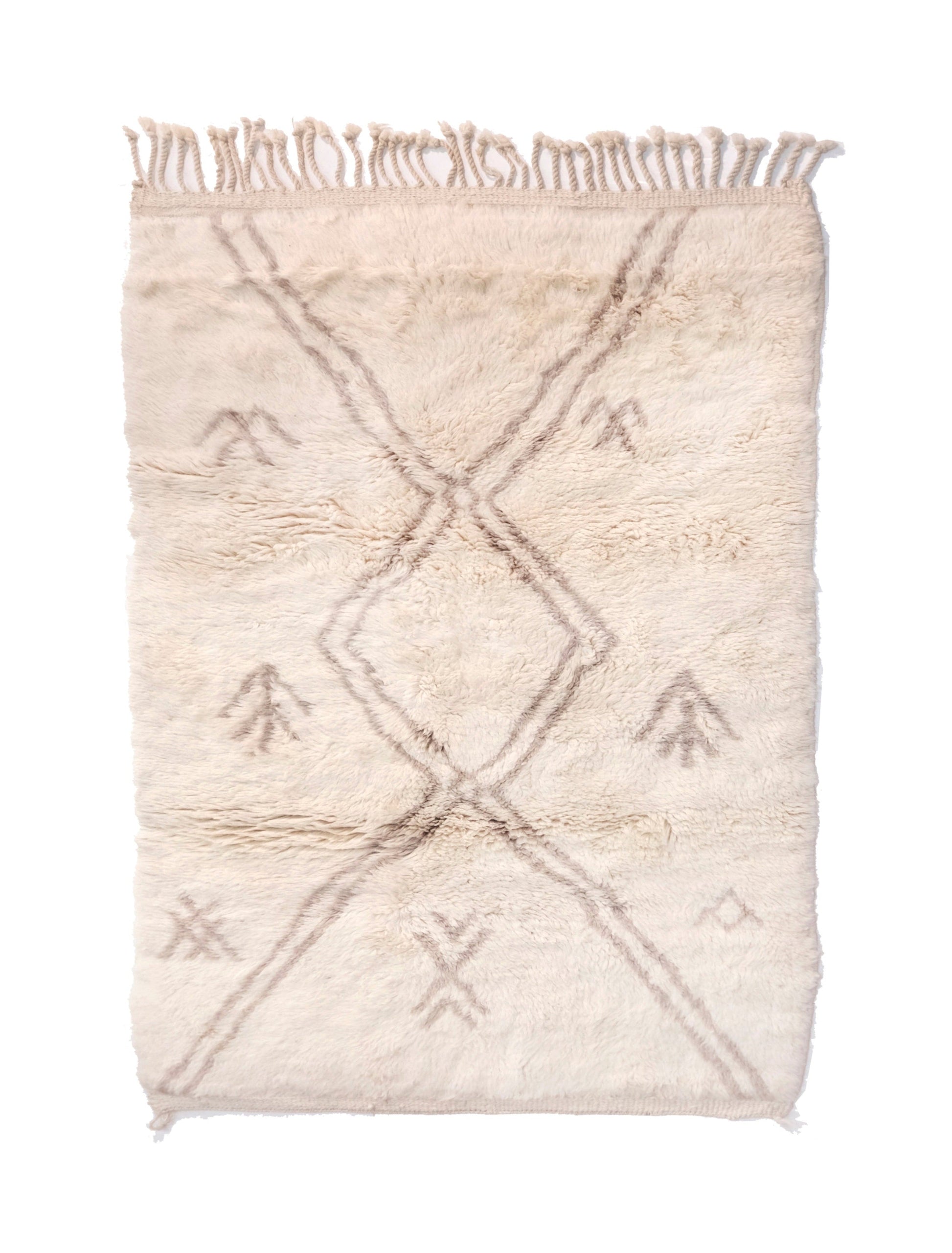 Plush cream wool Moroccan rug featuring a faded taupe geometric diamond lattice and scattered primitive tribal symbols, with a chunky top fringe and small braided bottom corner ties, displayed on a white background.

