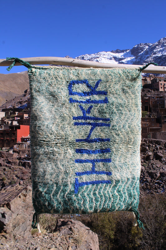 thinker rug, word art rug, beni ourain style, berber rug, moroccan rug, handmade rug, cooperative adrar, atlas mountains craft, artisanal rug, green wool rug, blue lettering rug, small accent rug, wall hanging rug, creative decor, boho decor, modern art rug, unique handmade rug, toubkal village craft, minimalist rug, studio decor